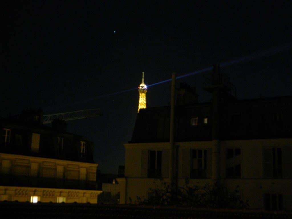 Twin beams rotate at the top of the Eiffel Tower at night.